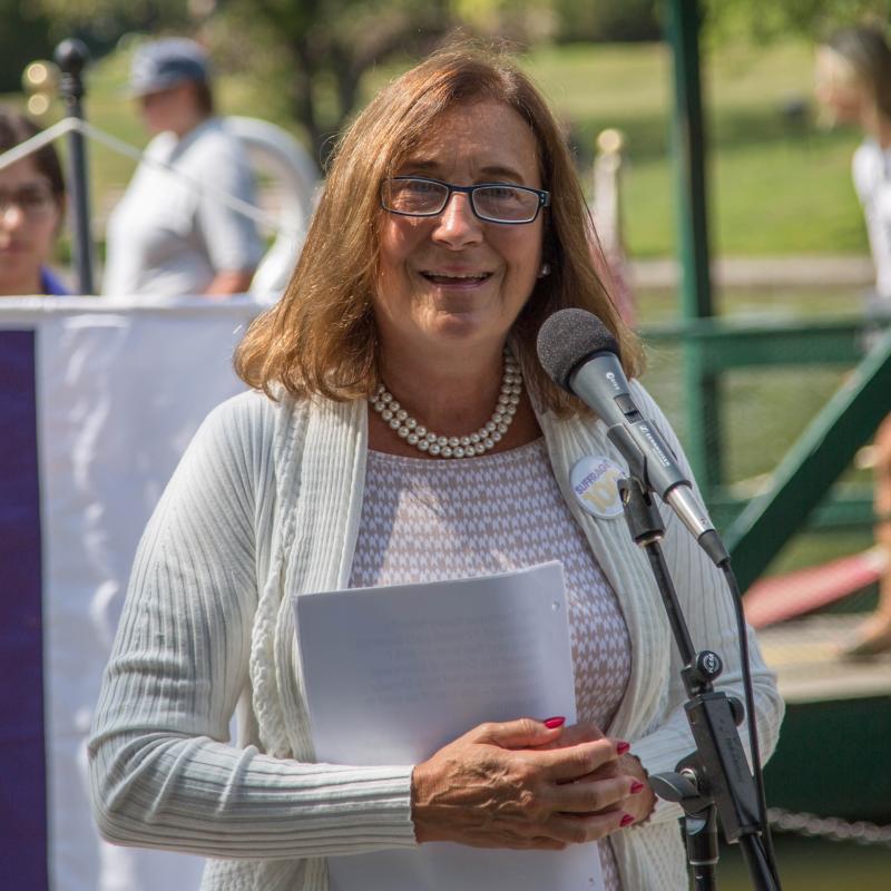 Woman speaks at microphone outside.