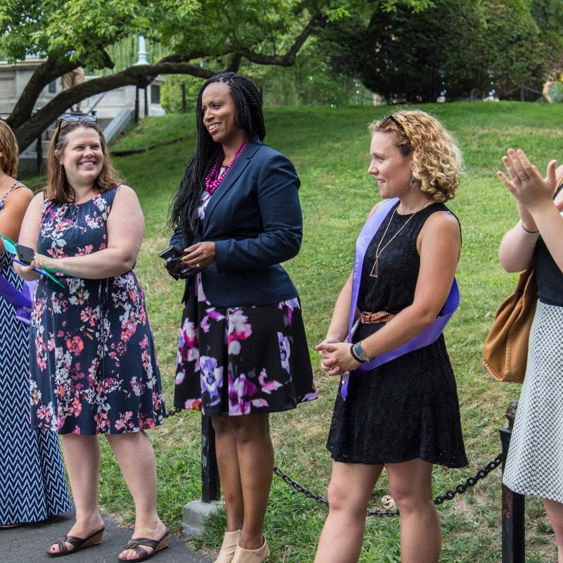 Five women stand outside applauding.