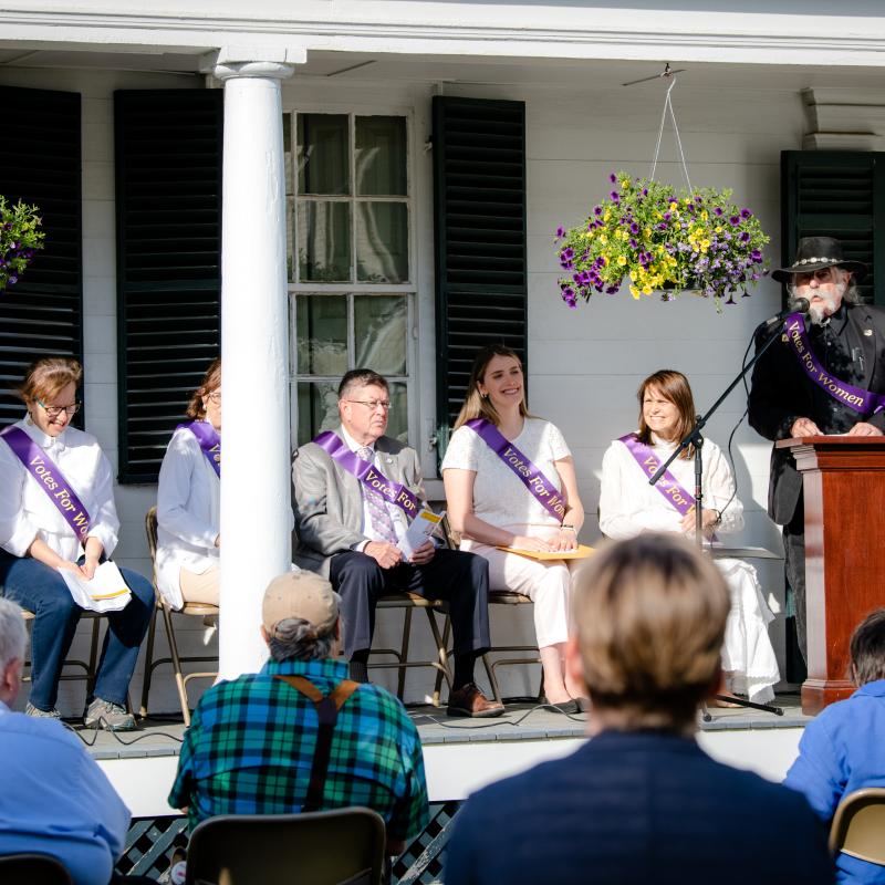 Group of people seated on front porch of house.