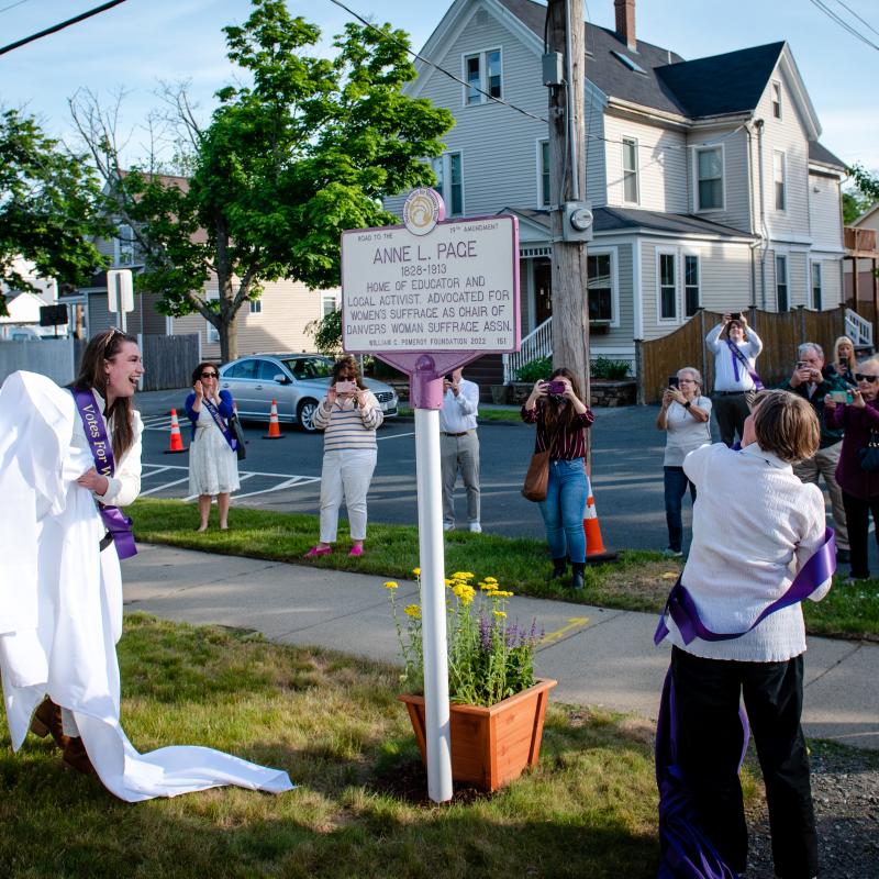 Woman pulls cloth off of purple and white sign.