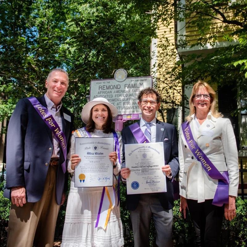 Four people in purple sashes stand outside.