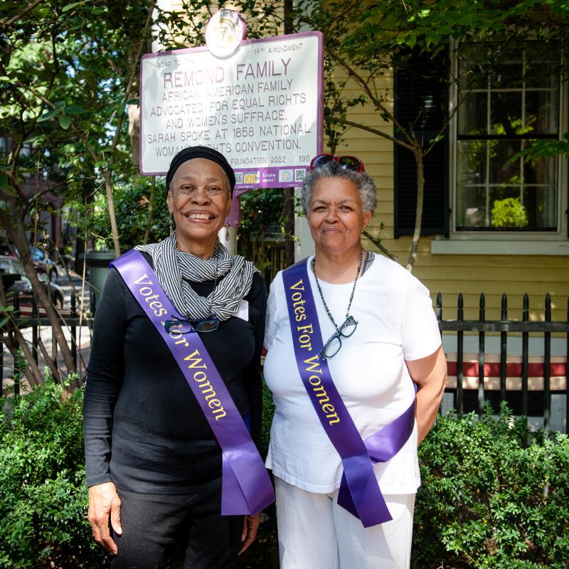 Two people stand in front of purple and white sign.