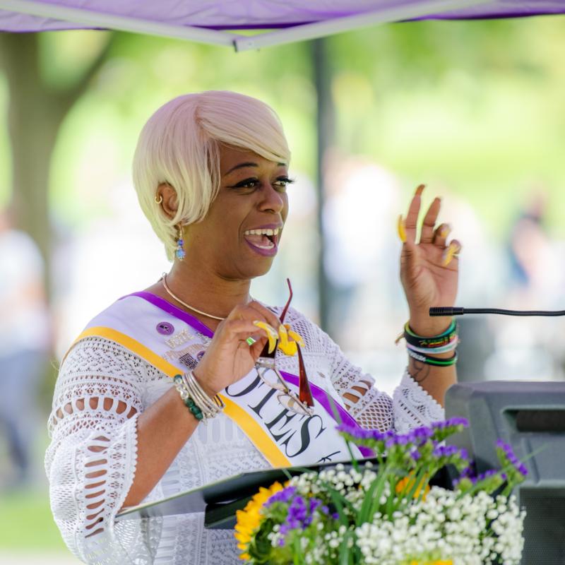 Woman wearing purple sash speaking at podium.