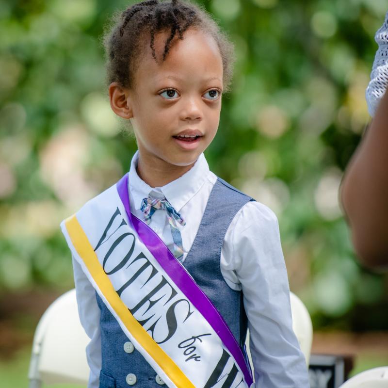 Girl stands outside wearing purple sash.