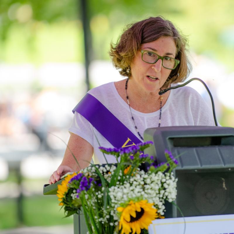 Woman wearing purple sash stands at podium.