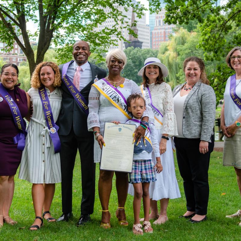 Group of people wearing purple sashes stand outside smiling.