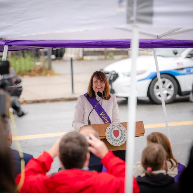 Crowd watches woman speaking at podium.