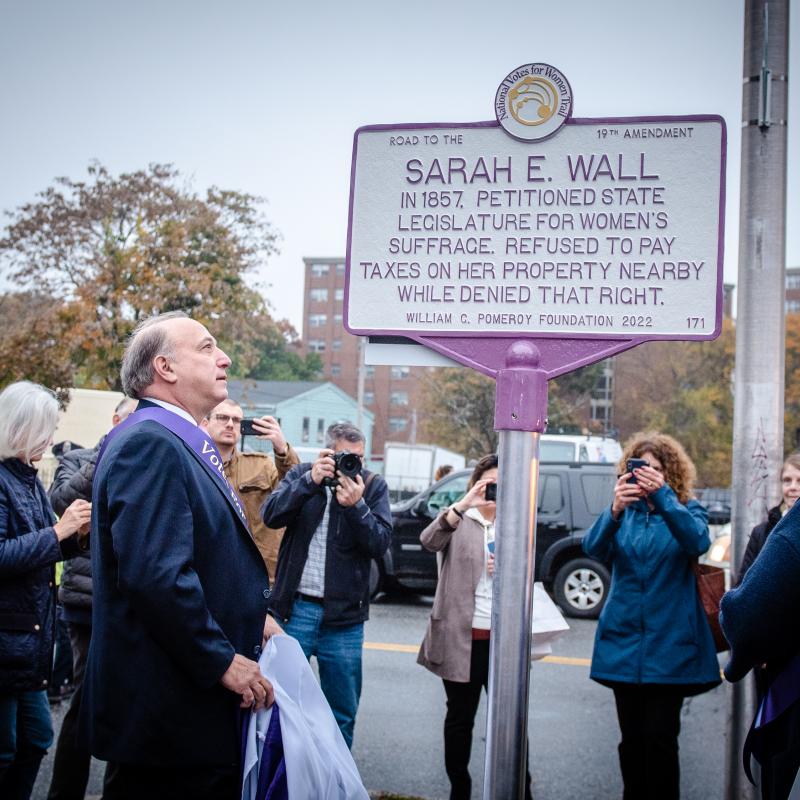 Crowd of adults looks up at sign.