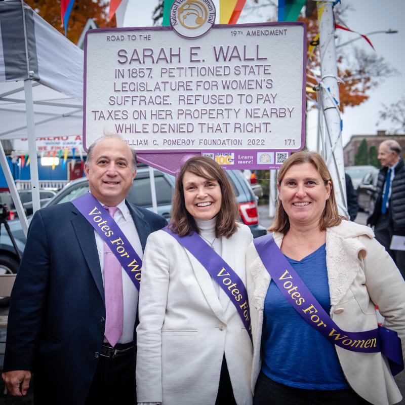 Three adults stand in front of sign.