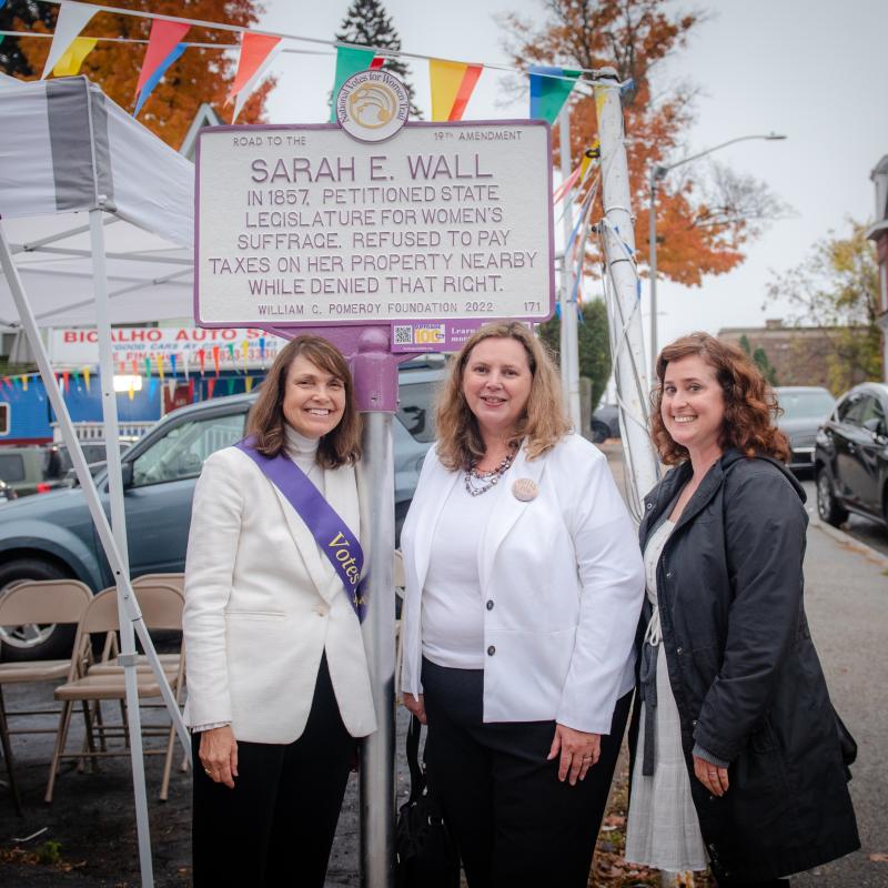 Three people stand in front of Sarah E. Wall suffrage marker.