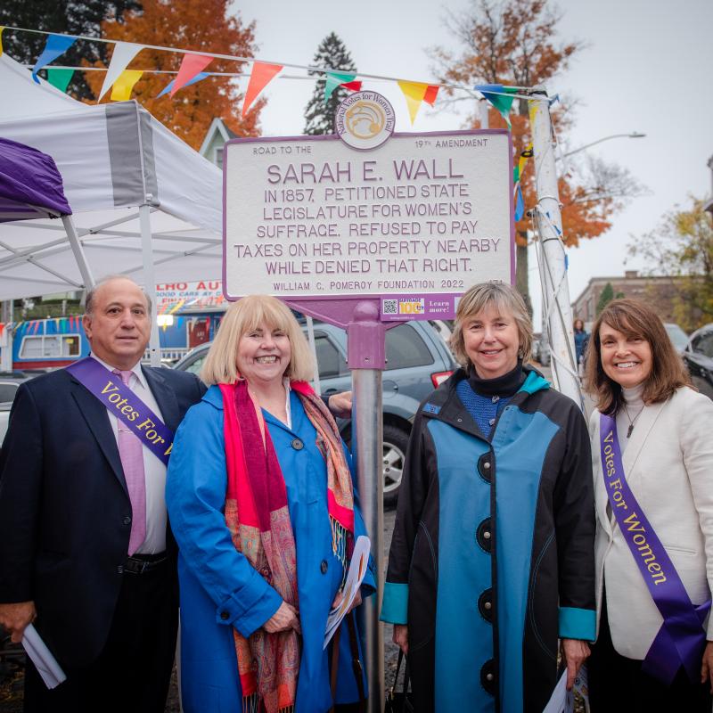 Five people stand in front of Sarah E. Wall suffrage marker.