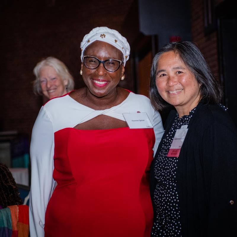 Two women stand indoors smiling.