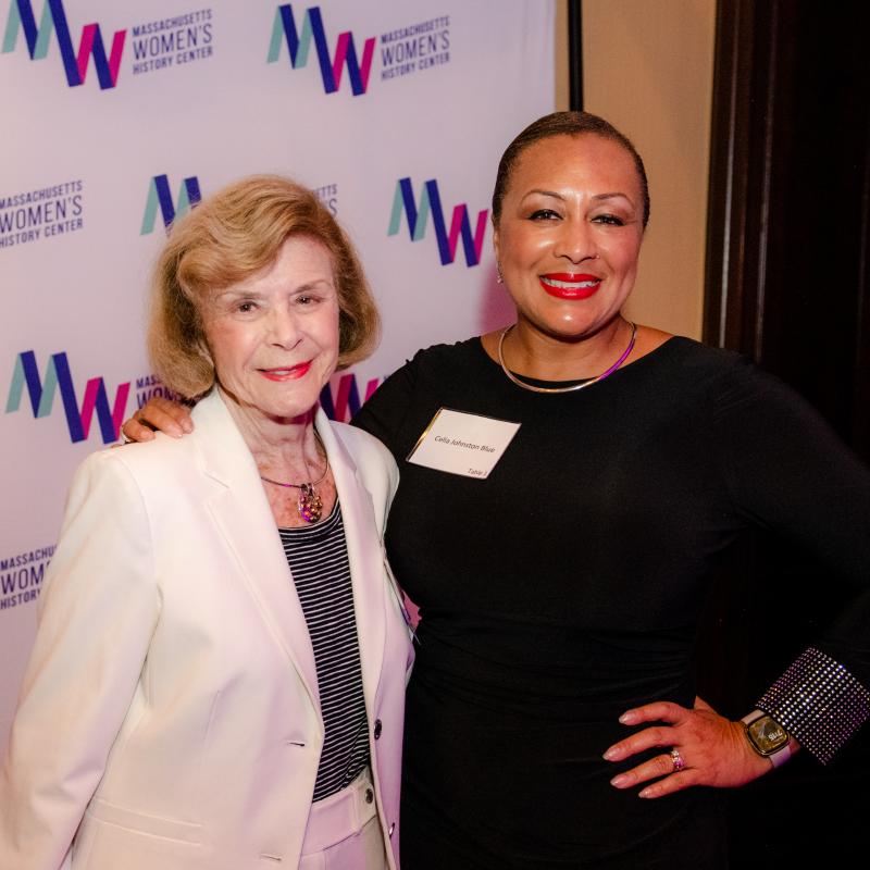 Two women stand in front of Massachusetts Women's History Center's step and repeat.