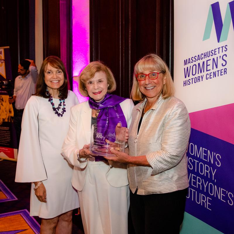 Three women stand in front of Massachusetts Women's History Center banner.