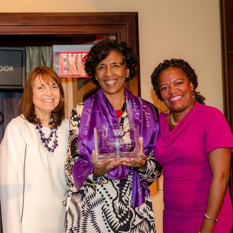 Three women stand indoors smiling.