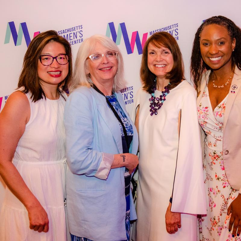 Four women stand in front of Massachusetts Women's History Center's step and repeat.