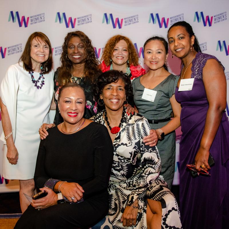 Group of women stand in front of Massachusetts Women's History Center's step and repeat.