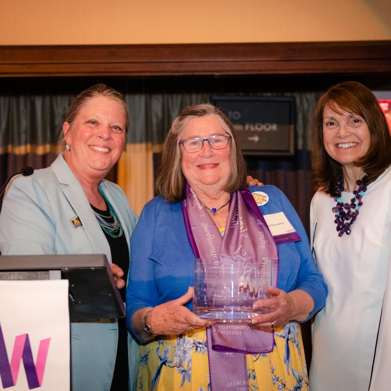 Three women stand on stage smiling.