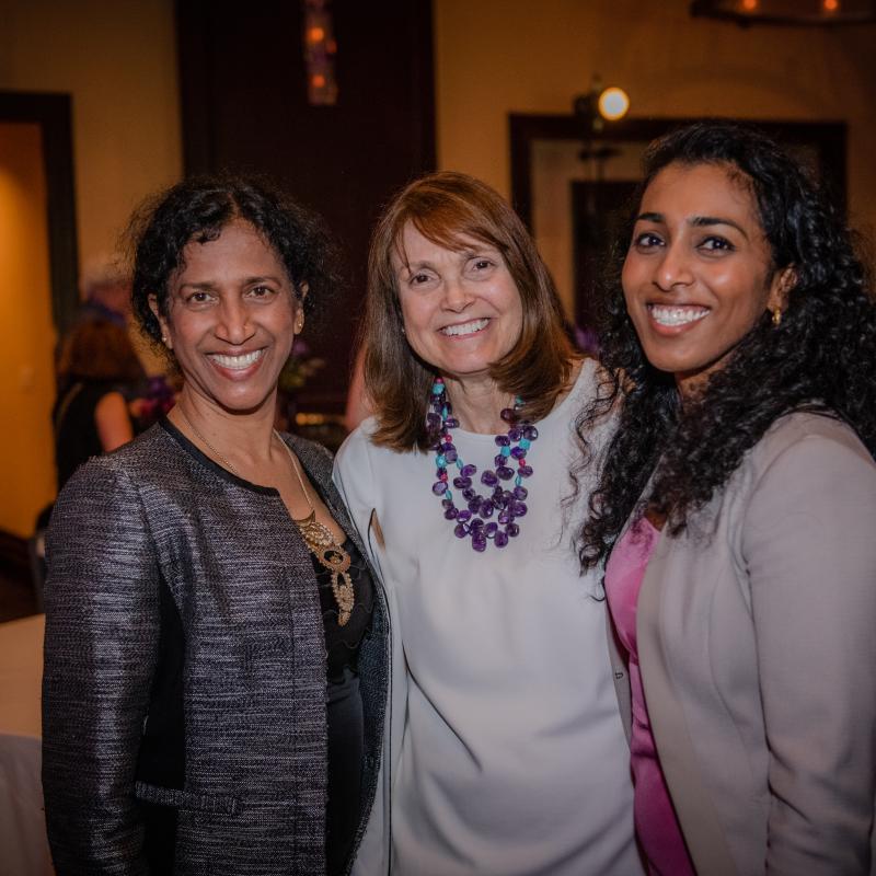 Three women stand indoors smiling.