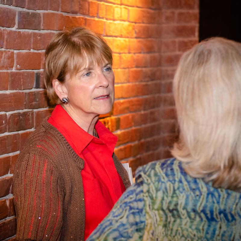 Martha Coakley stands indoors speaking to a woman.