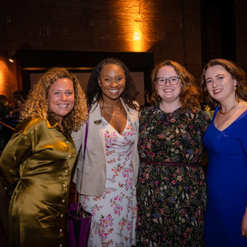 Four women stand indoors smiling.