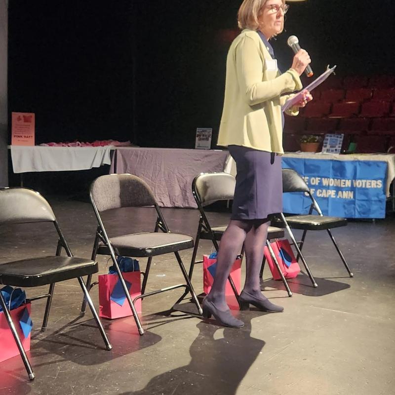 Woman stands on stage speaking into microphone.