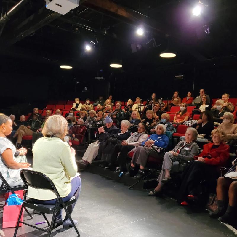 Group of people sit on stage speaking to crowd.