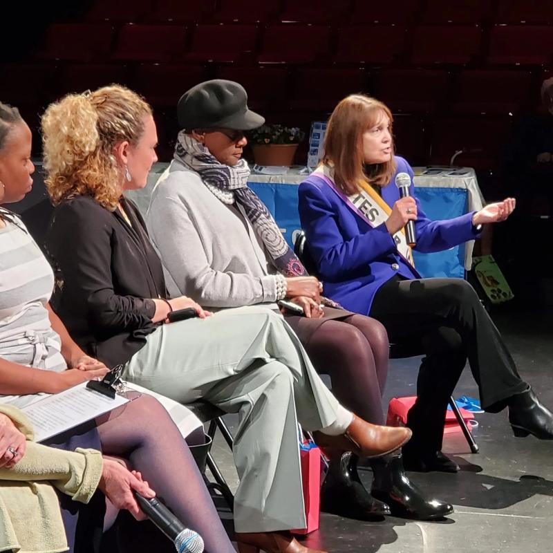 Group of people sit on stage speaking to crowd.