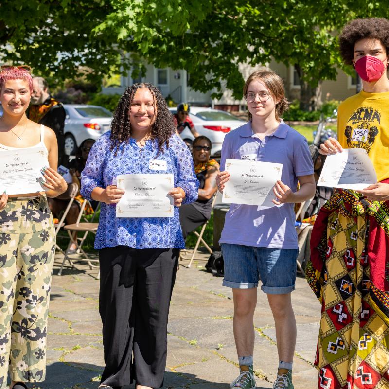 Four high school students stand outside holding certificates.