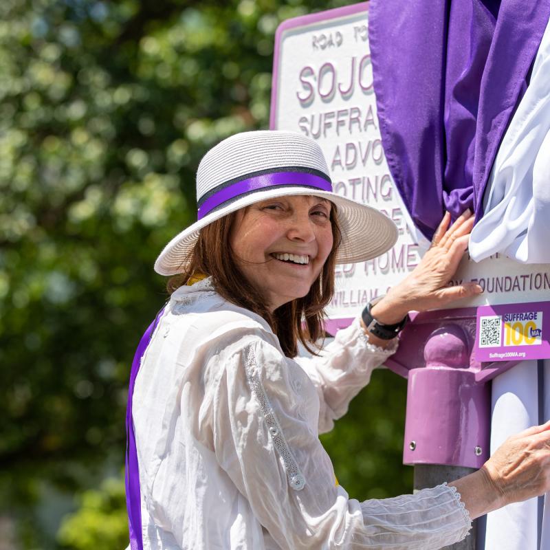 Woman in white stands outside smiling.