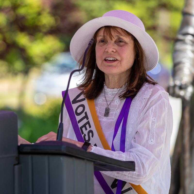 Woman wearing white speaks at podium.