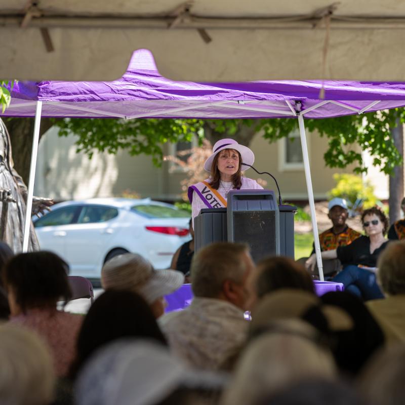 People sit outdoors under purple tent.