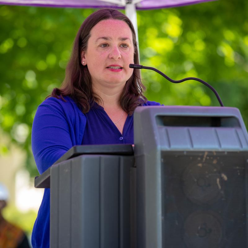 Woman wearing purple sash speaking at podium.