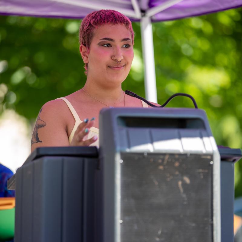 Woman wearing purple sash speaking at podium.