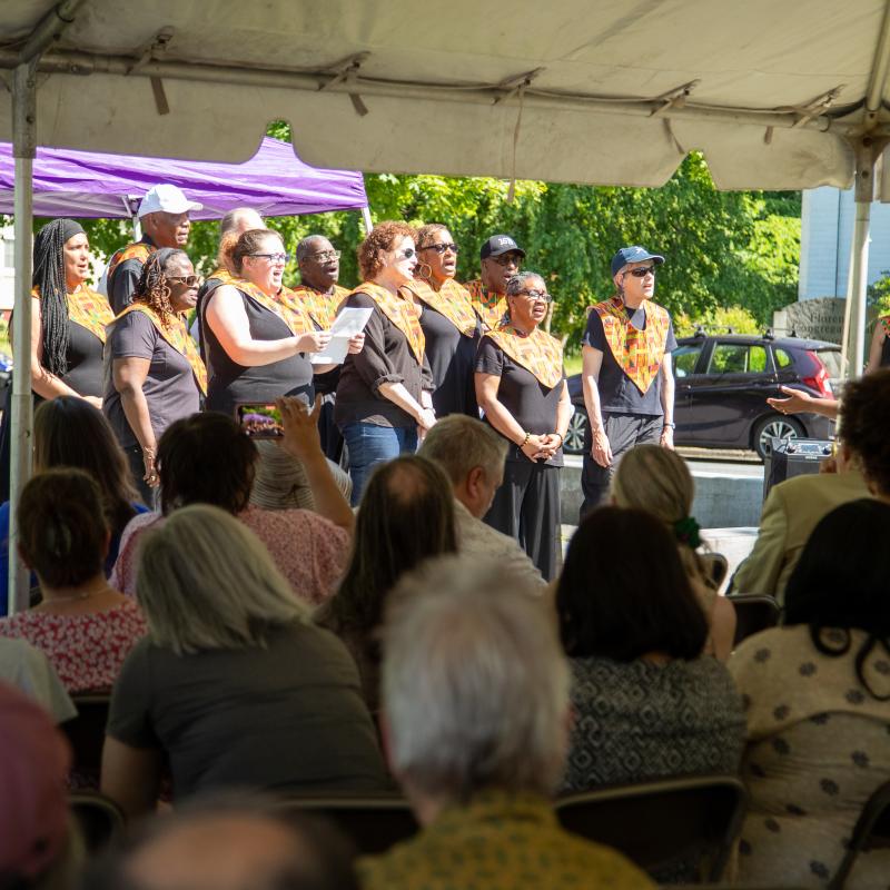 Group sits outdoors under purple tent.