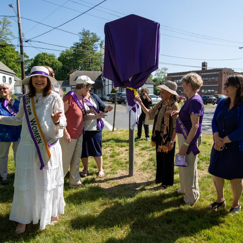 Group stands outside next to sign covered in purple cloth.