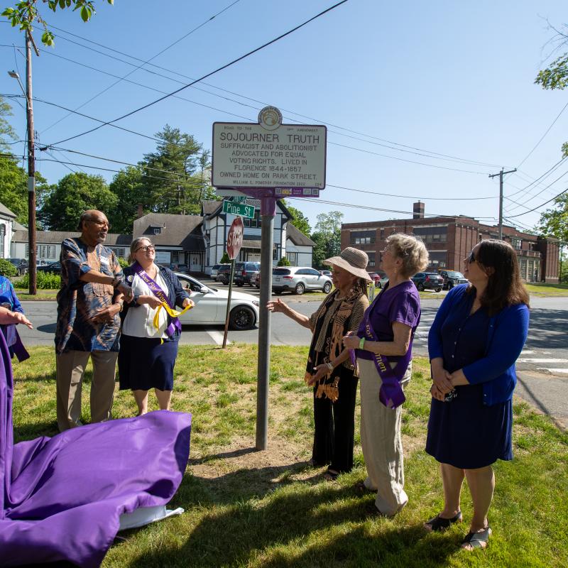 Group pulls covering off purple and white sign outdoors.