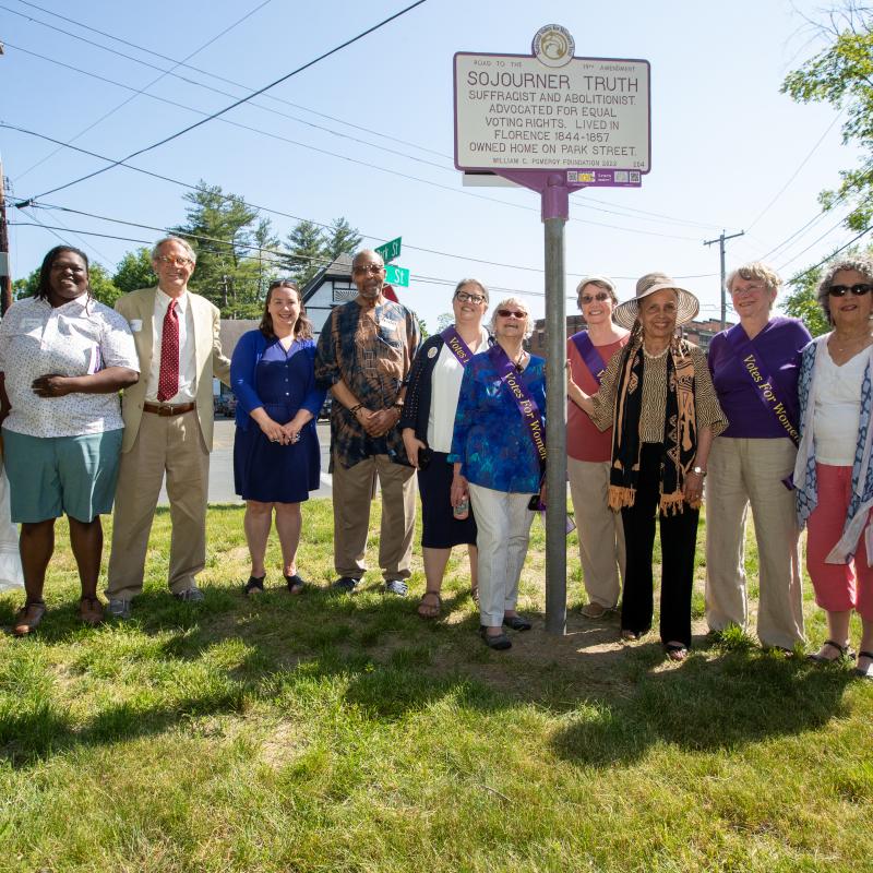 Group stands smiling outside next to Sojourner Truth marker.