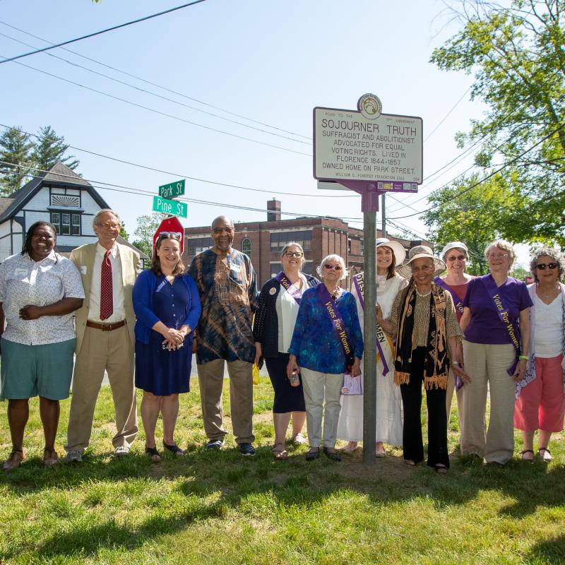 Group stands smiling outside next to Sojourner Truth marker.