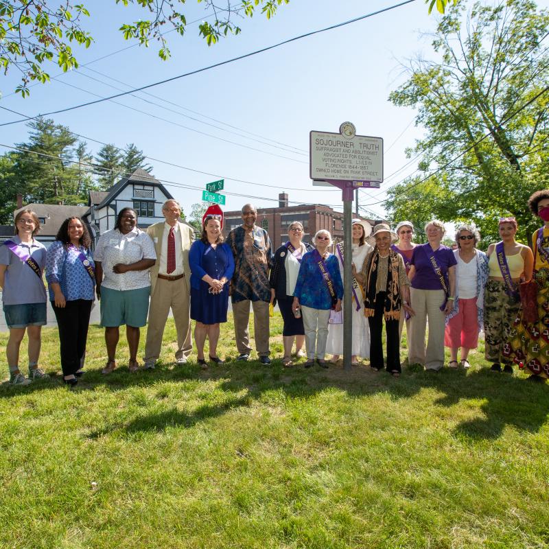 Group stands smiling outside next to Sojourner Truth marker.