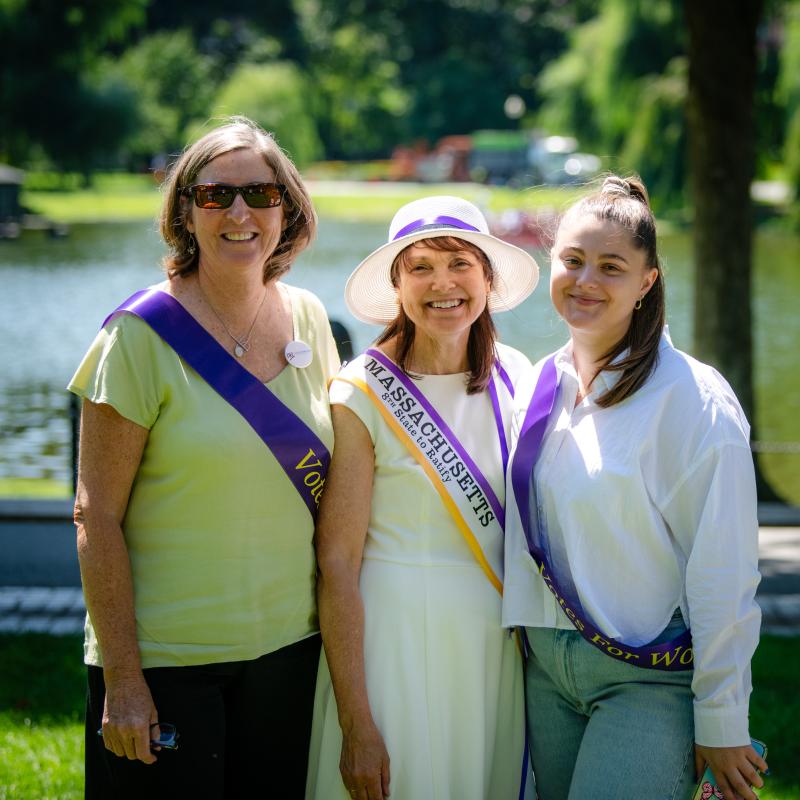Three women in purple sashes stand outside smiling.