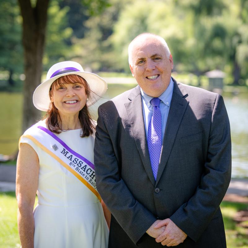 Man and woman in purple sashes stand outside smiling.