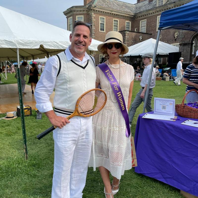 Man and woman wearing purple sash stand outside.