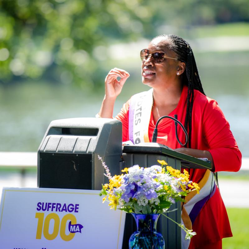 Woman wearing purple sash stands at podium.