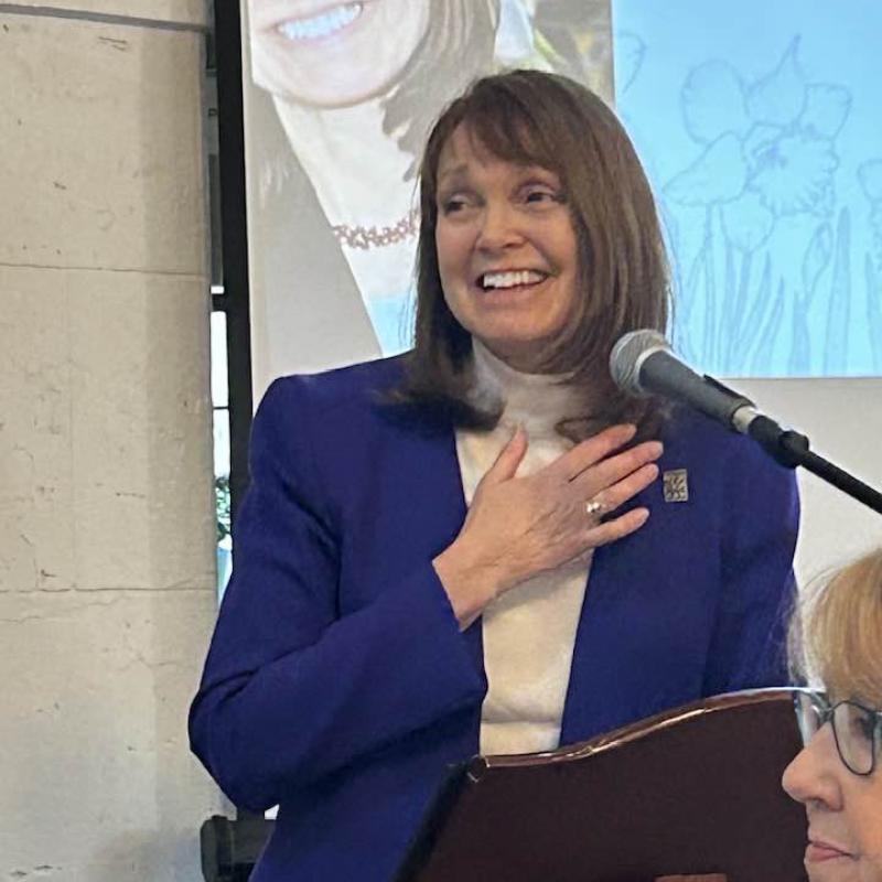 Woman stands indoors at podium smiling.