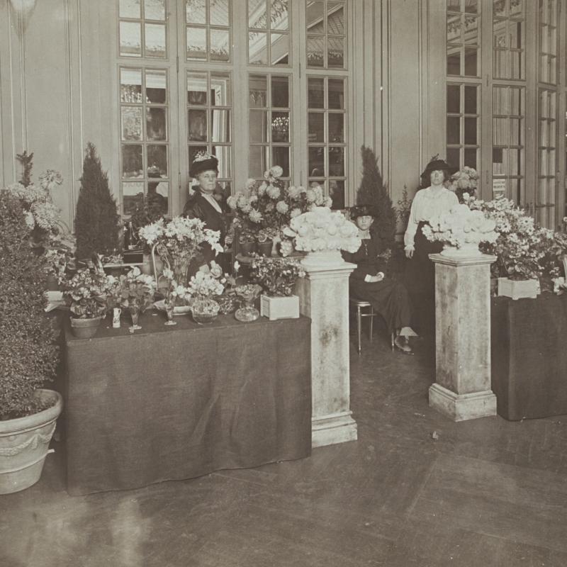 Black and white photograph of three women behind tables with flowers at a suffrage bazaar