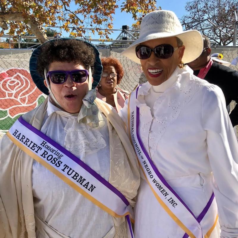 Two women in white wearing sashes.