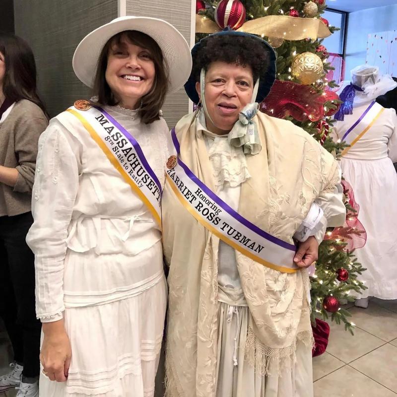 Two women in white wearing sashes.