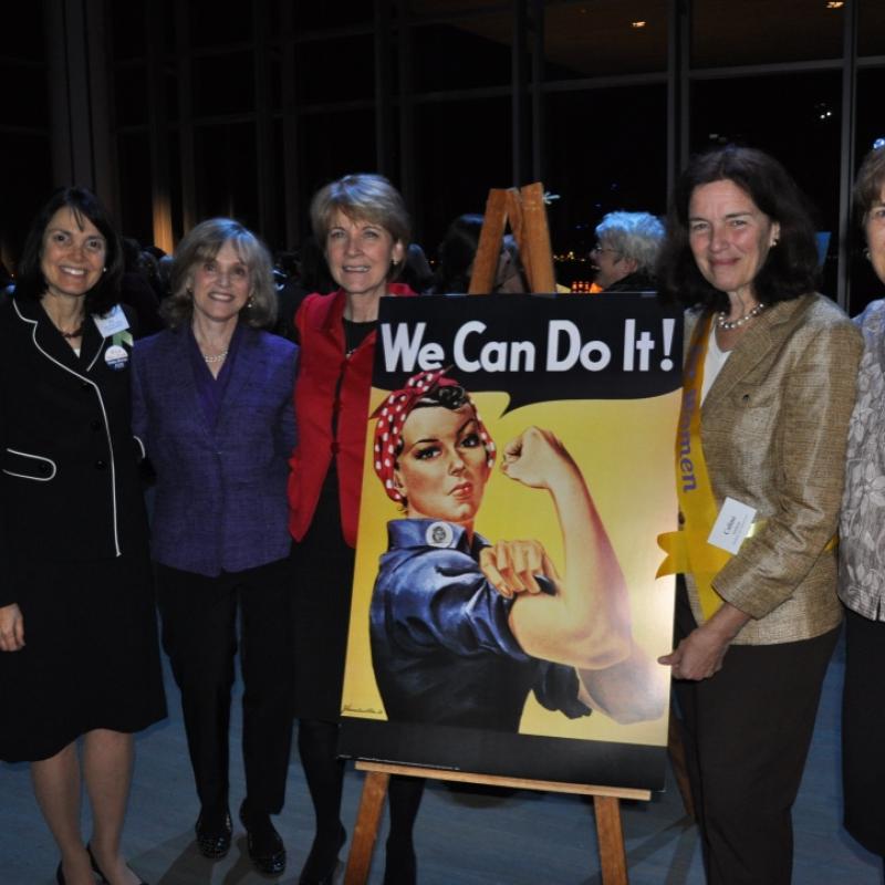 Five women stand next to Rosie the Riveter sign.