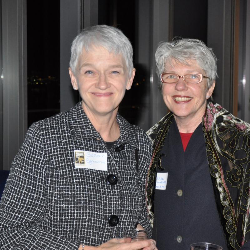 Two women stand indoors smiling.